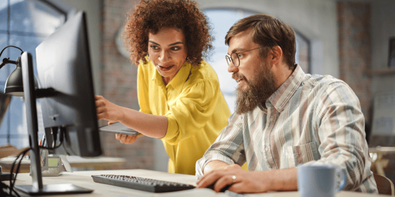 Eine Frau in gelbem Hemd zeigt einem Mann etwas auf einem Bildschirm beim Onboarding.