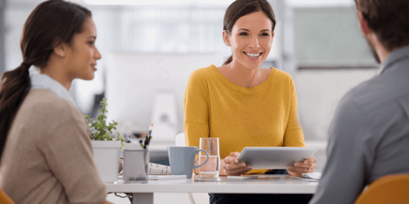 Frau im gelben Pullover hat mit zwei Personen ein Bewerbungsgespräch