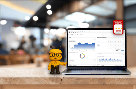 Ein Laptop steht auf einem Tisch, darauf sieht man das Cockpit der beesite. Die beeiste-biene zeigt auf den Bildschirm. Das Siegel 