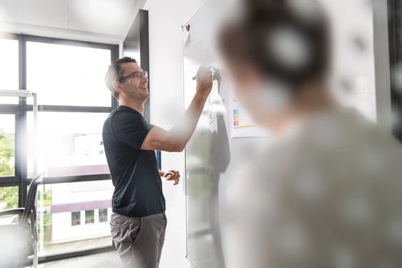 Lächelnder Mann am Whiteboard, der Recrutingprozesse skizziert