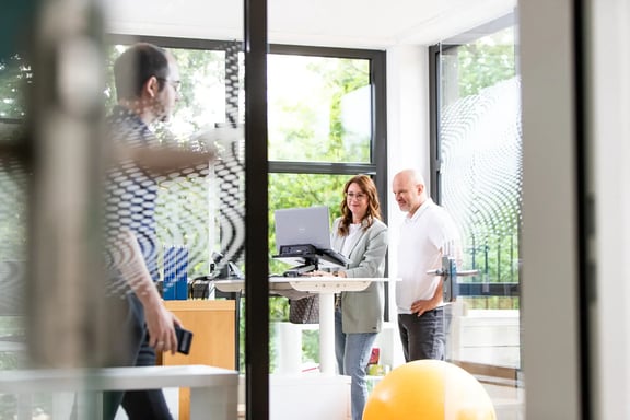 Eine Frau und ein Mann stehen an einem höhenverstellbaren Schreibtisch und schauen gemeinsam auf einen Laptop – Symbolbild für moderne HR-Softwarelösungen