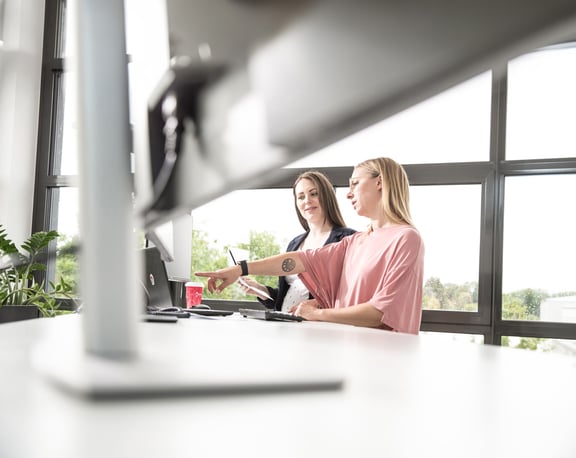 Zwei Frauen im Büro, eine zeigt auf den Laptop – Symbolbild für kollaborative Texterstellung mit KI