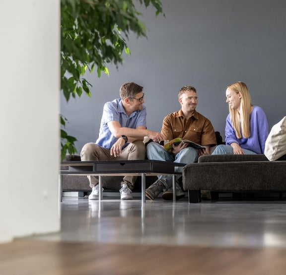 Drei Personen sitzen entspannt auf Sofas und unterhalten sich und lachen - Symbolbild für eine gute Teamarbeit