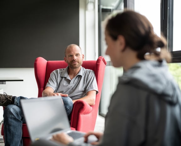Zwei Personen sitzen sich gegenüber, eine mit Laptop – Symbol für die schnelle Hilfe durch KI-gestützte Chatbots der beesite